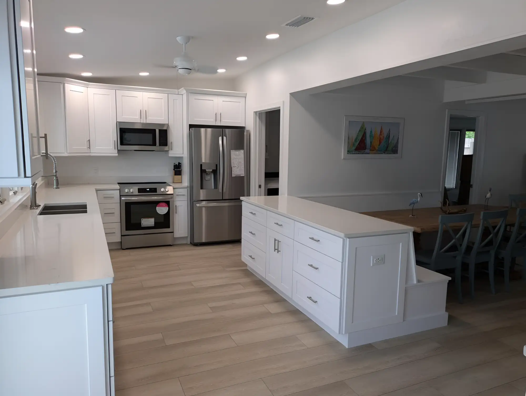 A bright remodelled kitchen with white shaker cabinets, quartz counters, a long island, a ceiling fan and a full grid of recessed cans.